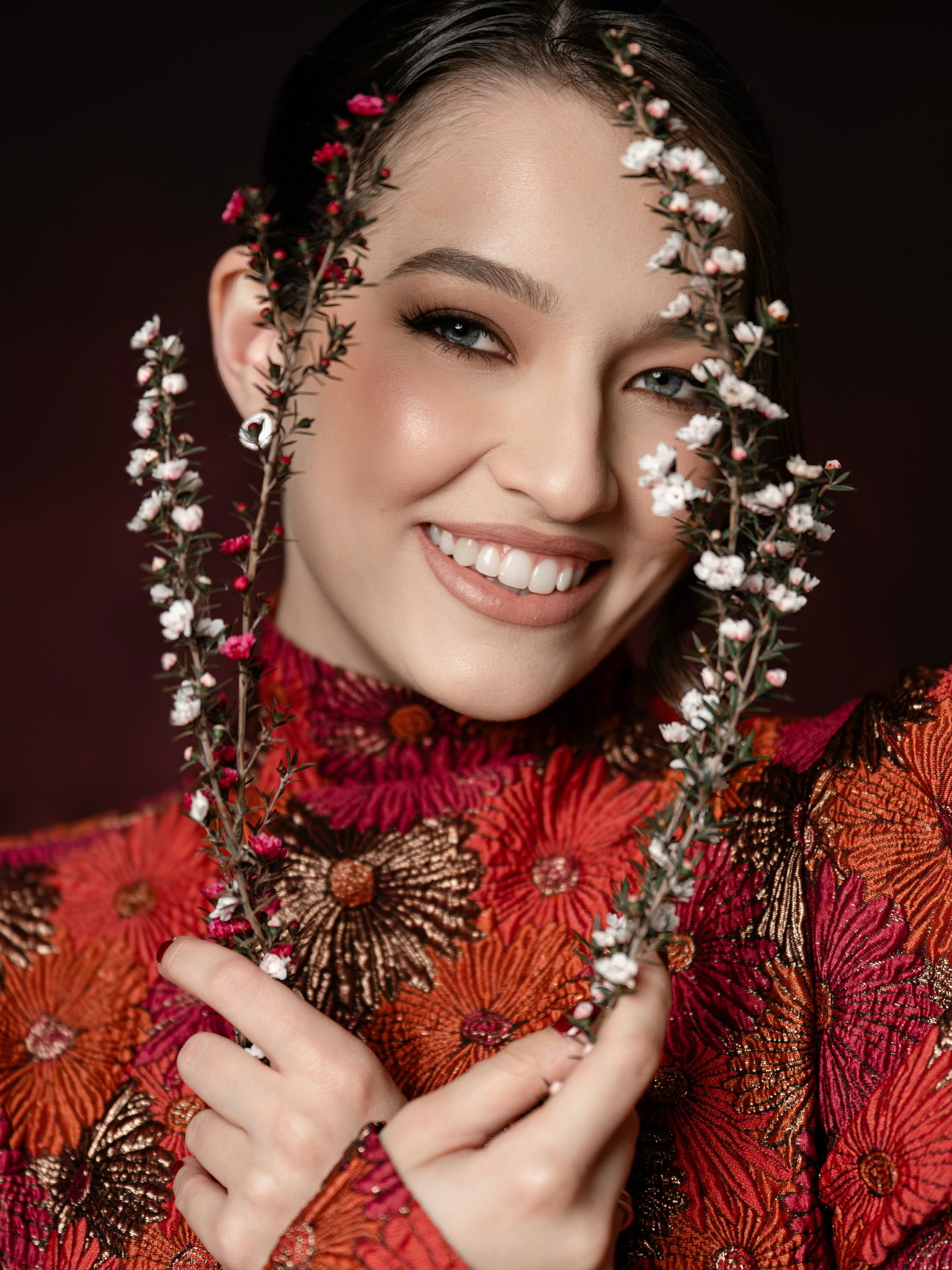 Jamilli sorrindo com flores brancas no cabelo, em ensaio editorial